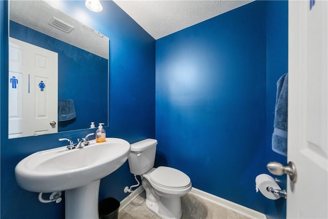 half bath with toilet, a textured ceiling, visible vents, and baseboards