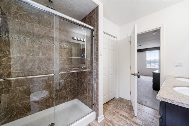 bathroom featuring double vanity, a stall shower, a sink, and a textured ceiling