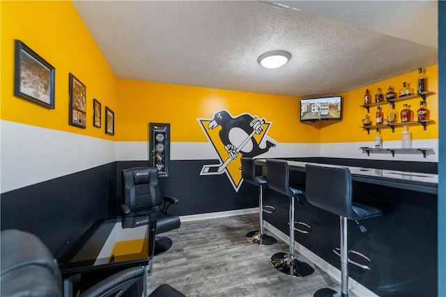 exercise room featuring a textured ceiling, baseboards, indoor wet bar, and wood finished floors