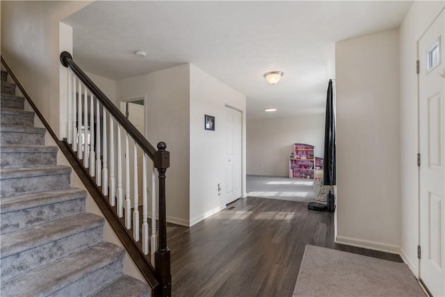 foyer entrance featuring dark wood finished floors, stairway, and baseboards