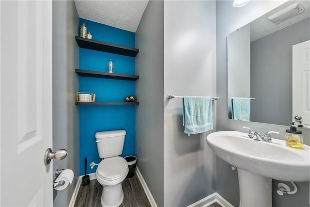 half bath featuring baseboards, visible vents, toilet, wood finished floors, and a textured ceiling