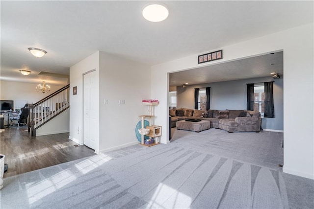 carpeted living area featuring stairs, wood finished floors, baseboards, and an inviting chandelier