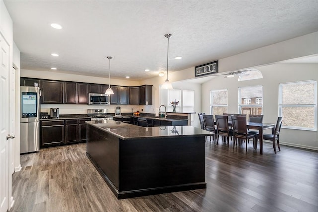 kitchen featuring dark brown cabinetry, dark countertops, dark wood-type flooring, stainless steel appliances, and pendant lighting