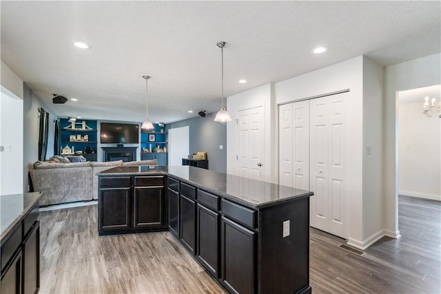 kitchen with a fireplace, a kitchen island, wood finished floors, visible vents, and open floor plan