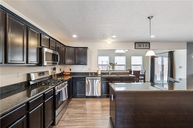 kitchen featuring dark brown cabinetry, light wood finished floors, dark stone countertops, stainless steel appliances, and a sink