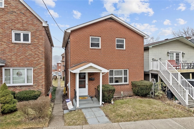 view of front of house with a wooden deck, a front yard, stairway, and brick siding