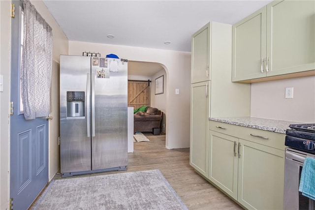 kitchen with arched walkways, light stone counters, appliances with stainless steel finishes, and light wood-style flooring