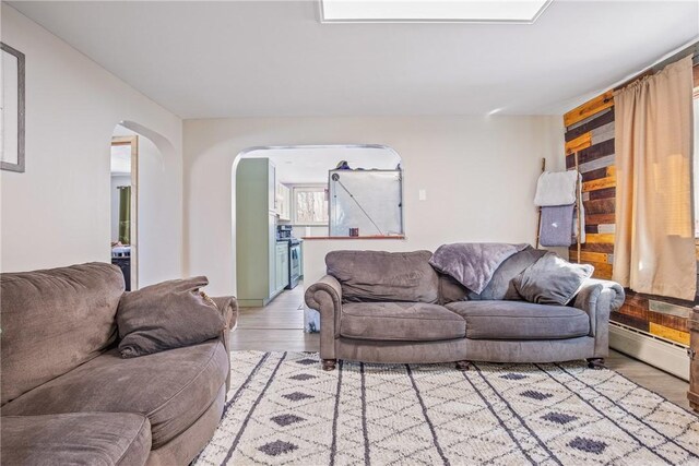 living area with arched walkways, light wood-style flooring, and a baseboard radiator