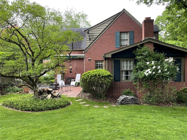 exterior space featuring brick siding, a shingled roof, a yard, a chimney, and a patio area