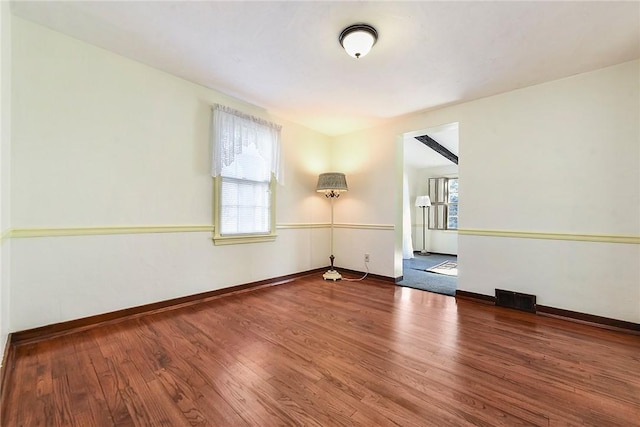empty room with a wealth of natural light, visible vents, baseboards, and wood finished floors