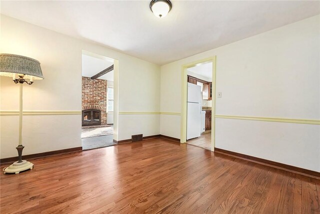empty room with a brick fireplace, visible vents, baseboards, and wood finished floors