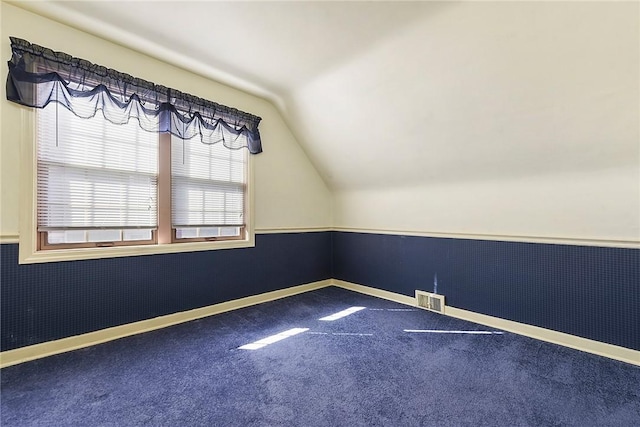carpeted empty room featuring lofted ceiling, wainscoting, visible vents, and baseboards