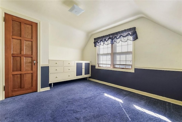 interior space featuring lofted ceiling, dark colored carpet, wainscoting, and baseboards
