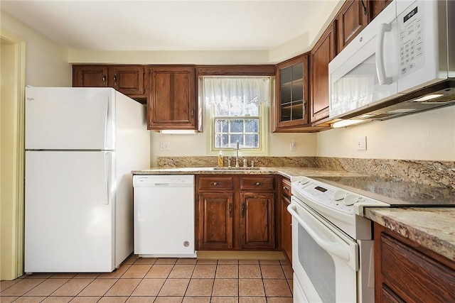 kitchen featuring glass insert cabinets, light tile patterned flooring, a sink, light stone countertops, and white appliances