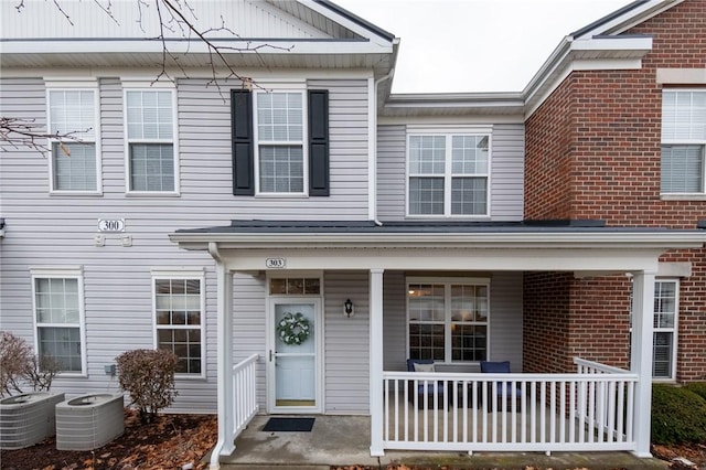 view of property featuring covered porch, brick siding, and cooling unit