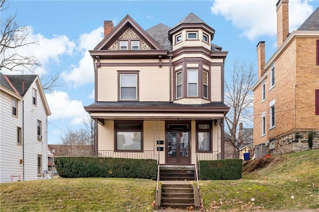 victorian home featuring covered porch, a front lawn, and a chimney