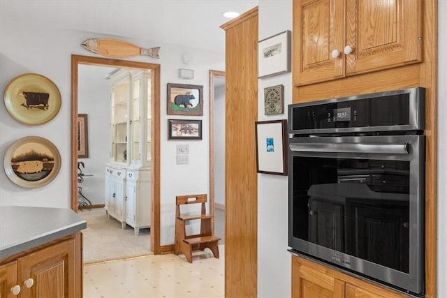 kitchen featuring light floors, double oven, baseboards, and brown cabinets