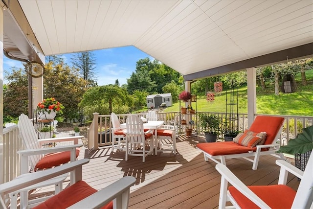 wooden deck with outdoor dining space, a lawn, and an outbuilding