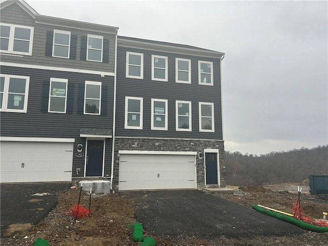 view of property with aphalt driveway, stone siding, and an attached garage