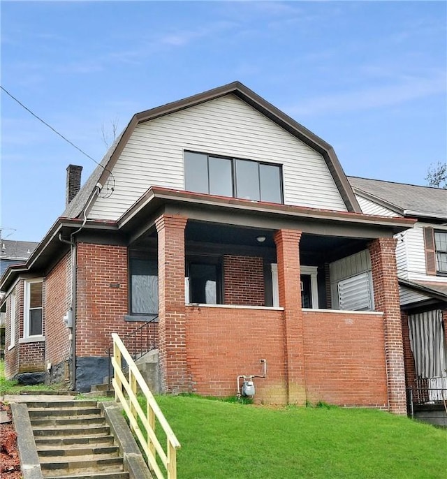 view of front of home with brick siding, a front yard, stairway, and a gambrel roof