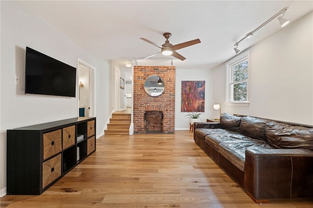 living room featuring baseboards, ceiling fan, rail lighting, light wood-type flooring, and a fireplace