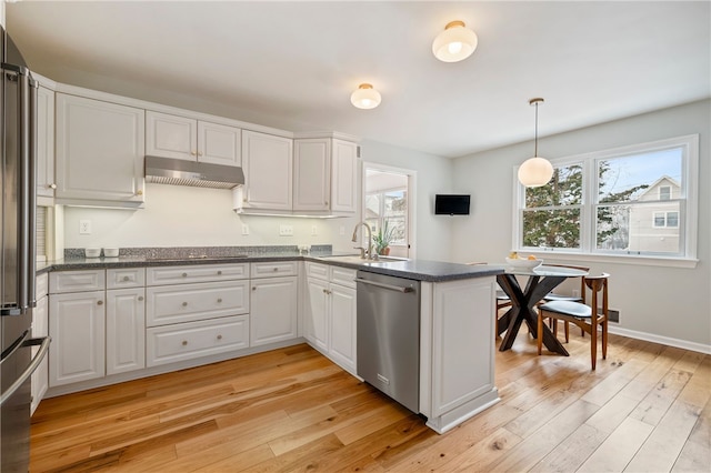 kitchen with under cabinet range hood, a peninsula, a sink, appliances with stainless steel finishes, and light wood finished floors