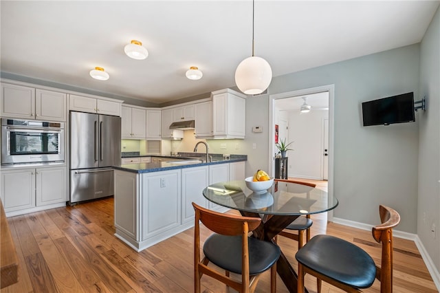 kitchen with under cabinet range hood, stainless steel appliances, a peninsula, baseboards, and light wood finished floors