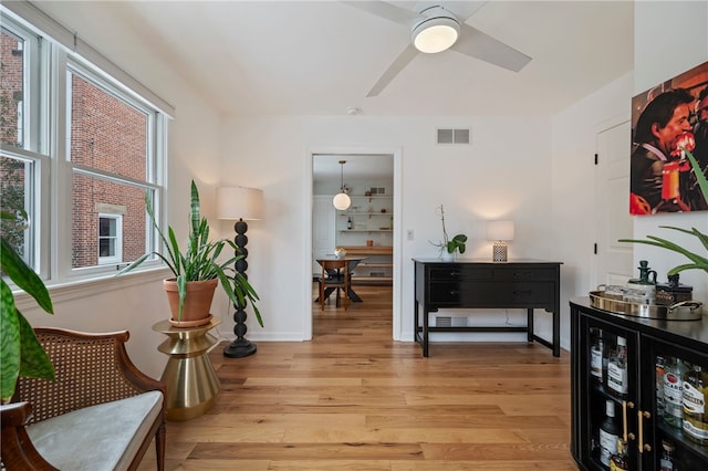 living area with a ceiling fan, light wood-type flooring, visible vents, and baseboards