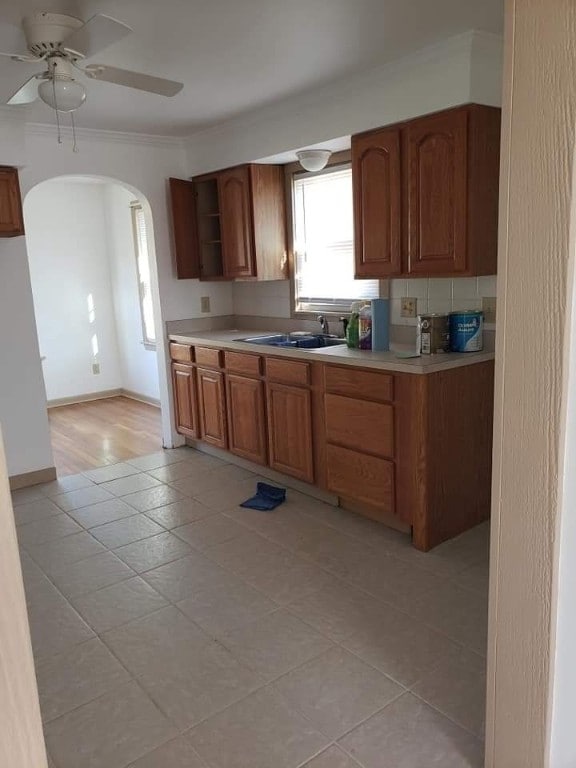 kitchen with arched walkways, ceiling fan, a sink, light countertops, and crown molding