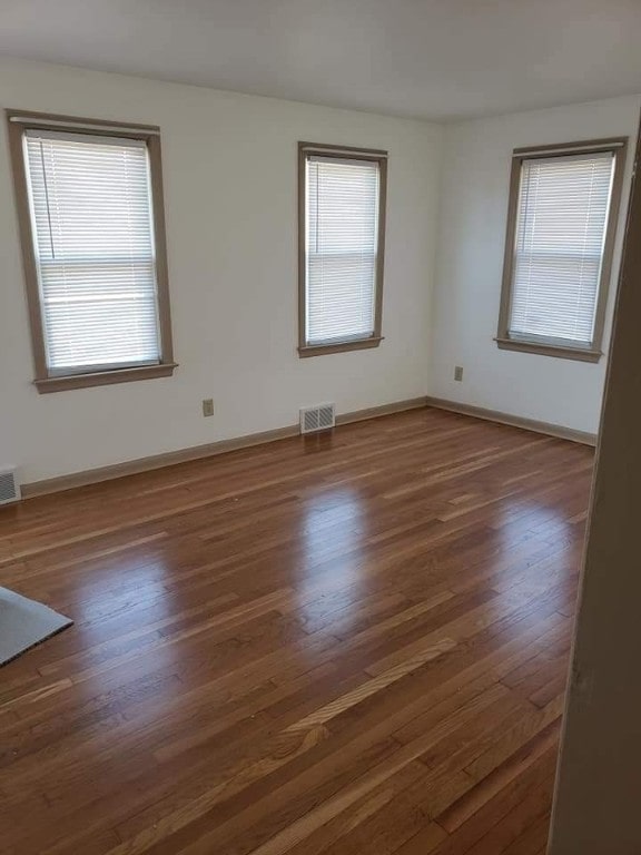 unfurnished room featuring visible vents, baseboards, and wood finished floors