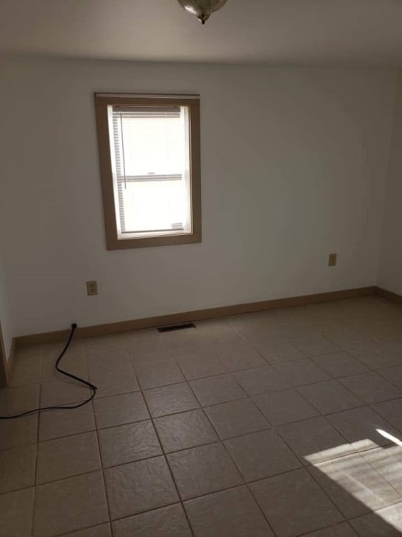 spare room featuring light tile patterned flooring, visible vents, and baseboards