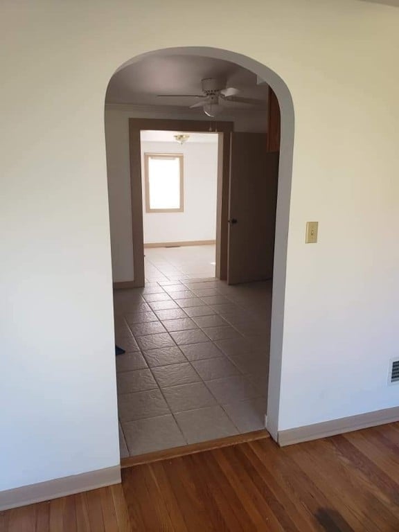 corridor featuring arched walkways, baseboards, and wood finished floors