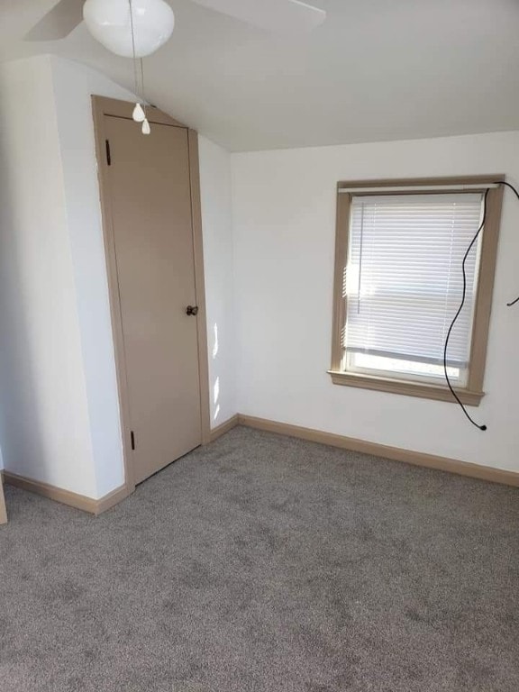 carpeted empty room featuring lofted ceiling and baseboards