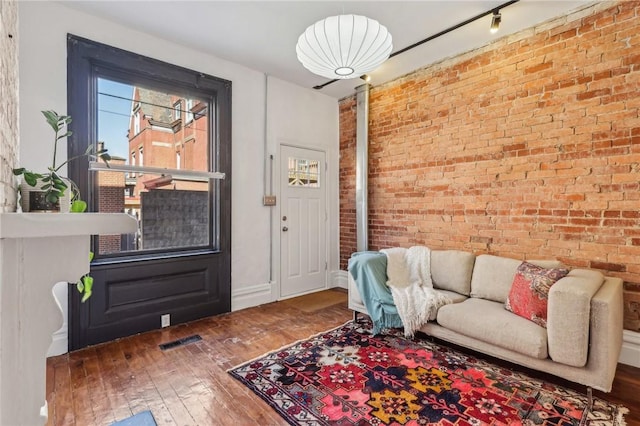 living area with hardwood / wood-style flooring, brick wall, visible vents, baseboards, and rail lighting