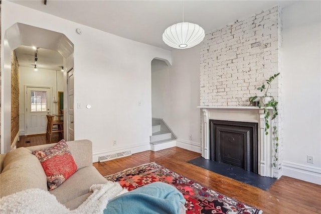 living room featuring arched walkways, a glass covered fireplace, wood finished floors, and visible vents