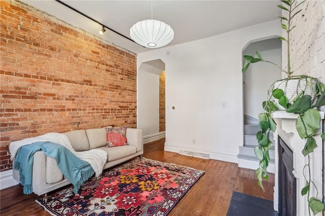 living area featuring baseboards, visible vents, arched walkways, brick wall, and hardwood / wood-style floors