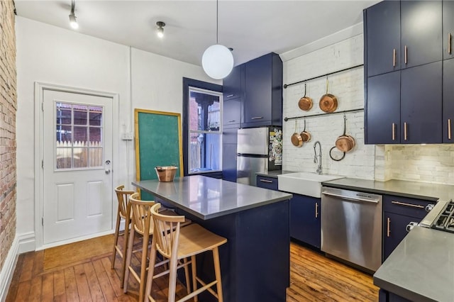 kitchen with hardwood / wood-style flooring, appliances with stainless steel finishes, blue cabinetry, a kitchen bar, and a sink