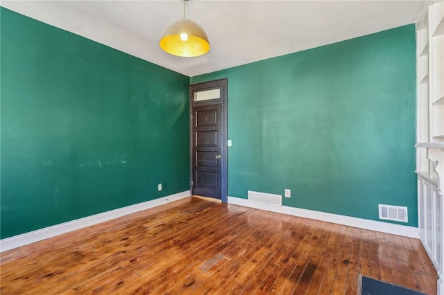 spare room featuring wood-type flooring, visible vents, and baseboards