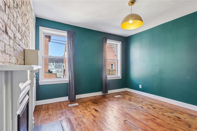 spare room with baseboards, visible vents, hardwood / wood-style floors, and a fireplace with flush hearth