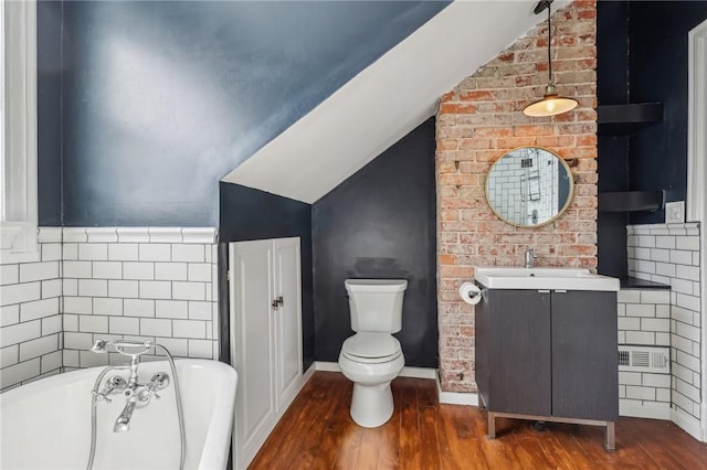 bathroom featuring lofted ceiling, toilet, vanity, wood finished floors, and a freestanding tub