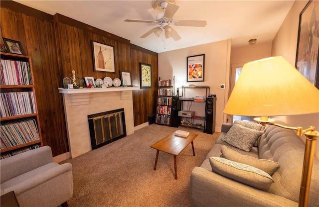 living area featuring a brick fireplace, wooden walls, a ceiling fan, and carpet flooring