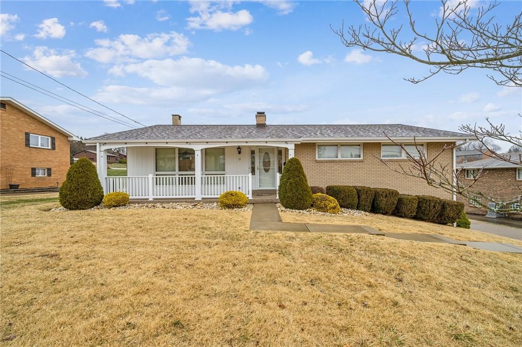 ranch-style home with a chimney, a front lawn, a porch, and brick siding