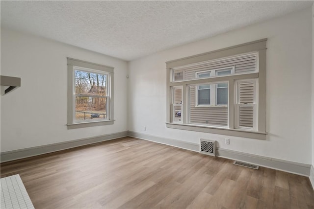 unfurnished room featuring baseboards, a textured ceiling, visible vents, and wood finished floors