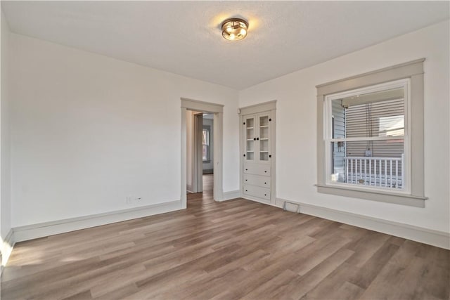 empty room with visible vents, a textured ceiling, baseboards, and wood finished floors