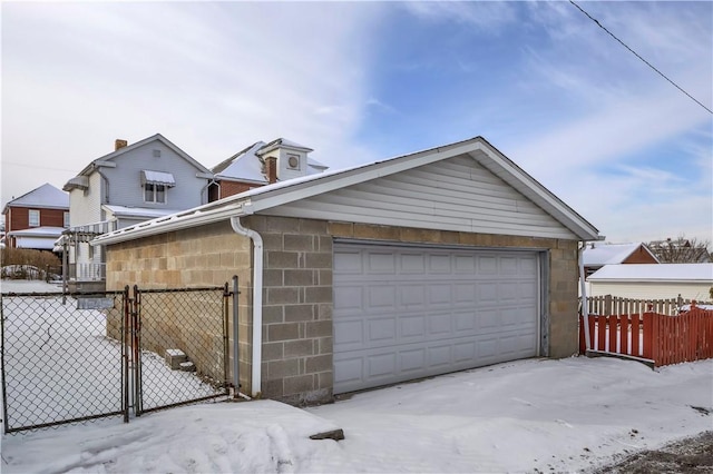 snow covered garage with a gate, a detached garage, and fence