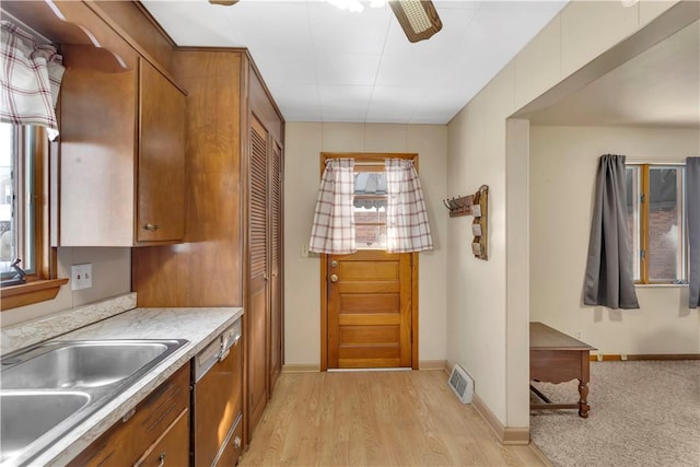 kitchen featuring a sink, light wood-style floors, light countertops, stainless steel dishwasher, and brown cabinets