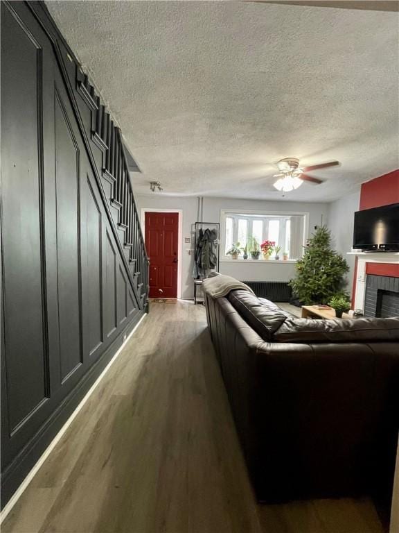 living room featuring a textured ceiling, a tile fireplace, wood finished floors, a ceiling fan, and stairway