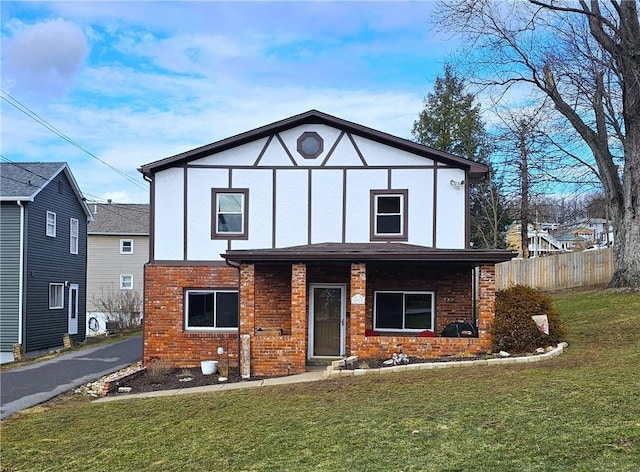 tudor-style house featuring a front lawn, fence, and brick siding