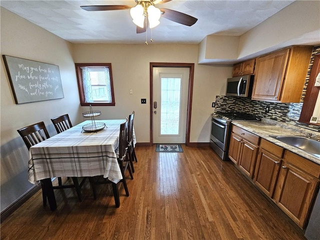 kitchen featuring dark wood-style floors, stainless steel appliances, tasteful backsplash, brown cabinetry, and a sink