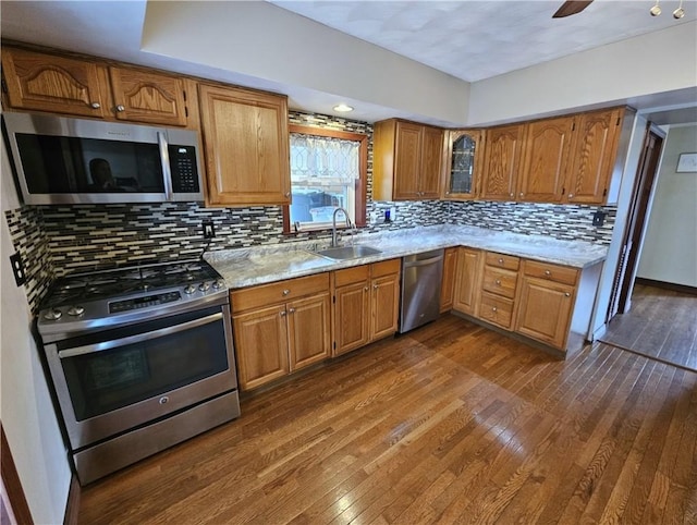 kitchen with brown cabinetry, glass insert cabinets, appliances with stainless steel finishes, dark wood-type flooring, and a sink